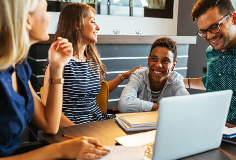 A group of people sitting around a table with a laptop.