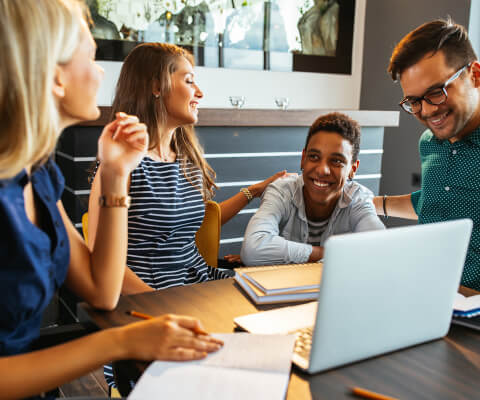 A group of people sitting around a table with a laptop.