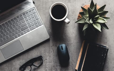 A laptop on a table next to a plant and glasses.