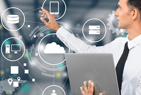 A man with a laptop in front of a server room.