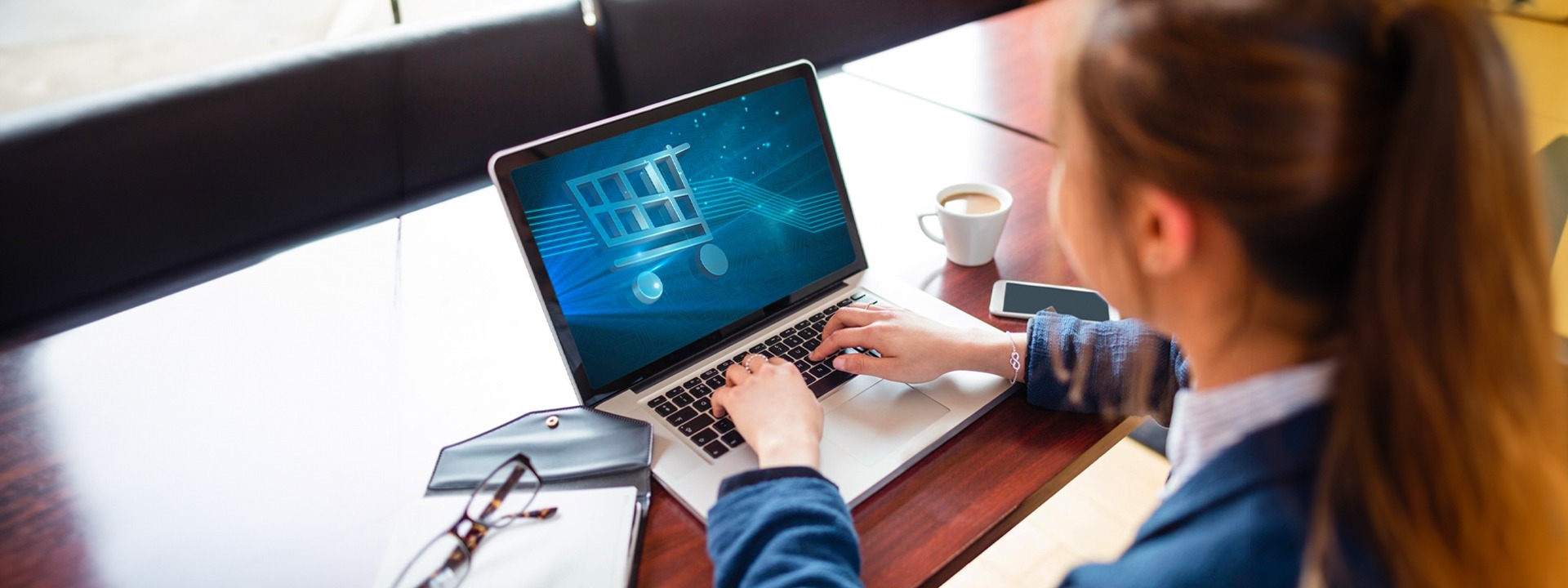 A woman using a laptop with a shopping cart on it.