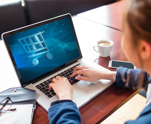 A woman using a laptop with a shopping cart on it.